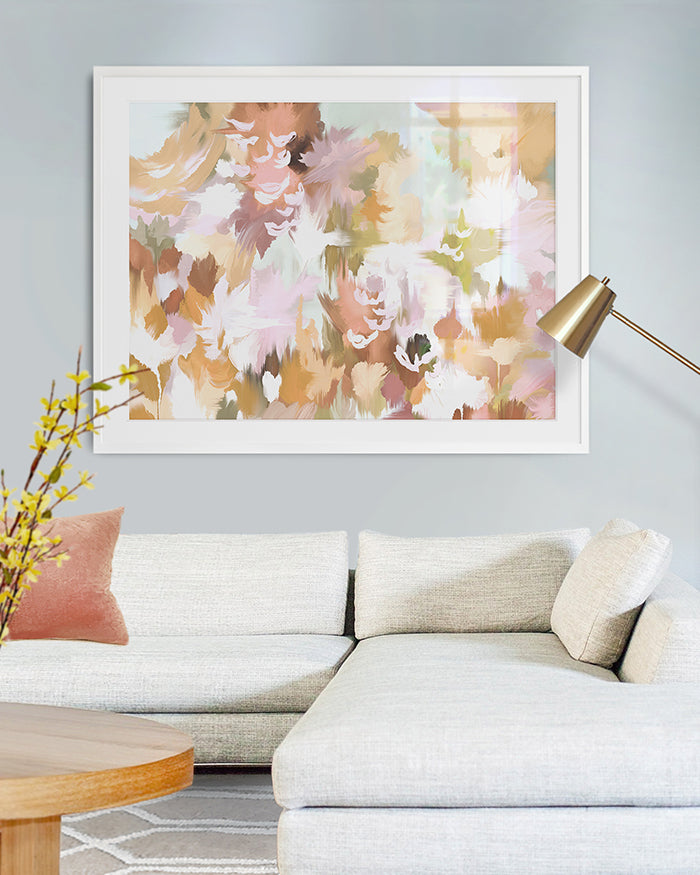 A living room featuring a large, abstract art in golden yellows, lilac pinks, greens, orange and browns.
The artwork is framed and showcased on a light grey wall above a white sectional sofa. There is a round, modern coffee table and a gold floor lamp next to it.