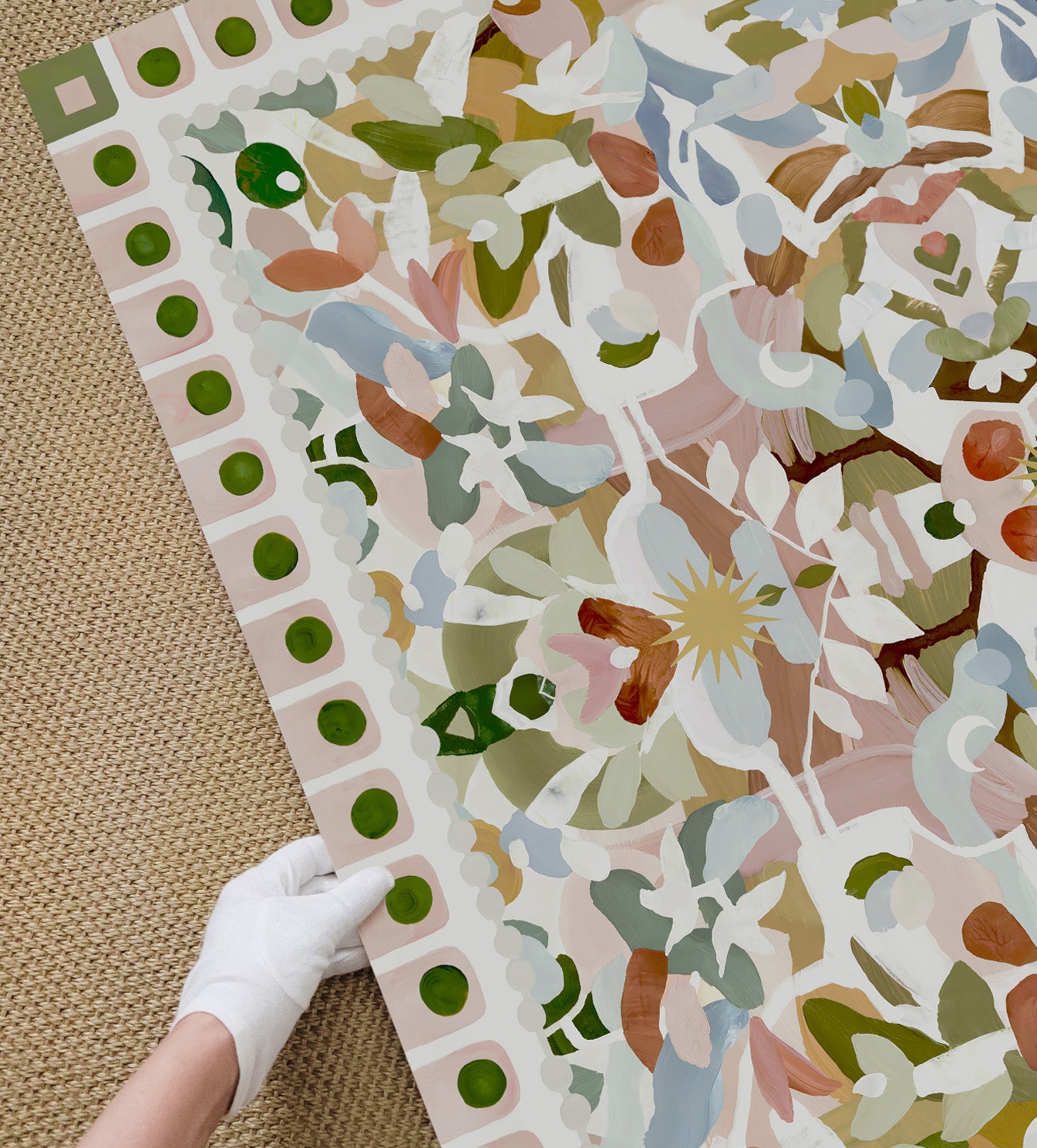 Close-up view of colorful art in light greens, pinks and blues being held by a gloved hand on a textured surface