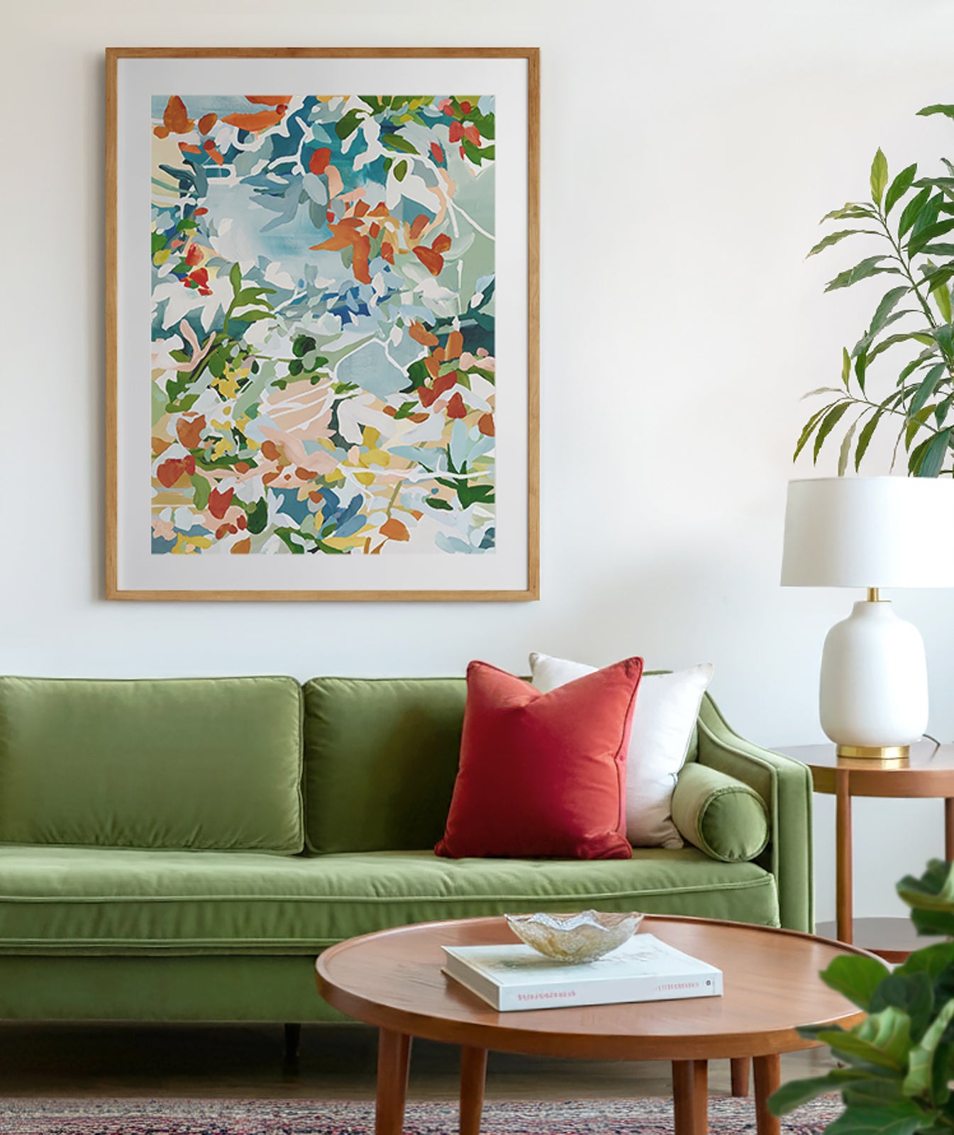 A mid century modern living room with velvet green sofa and red and white cushions, there is a traditional red carpet and round, wooden coffee table. The art is a floral abstract with warm reds, greens and blues.