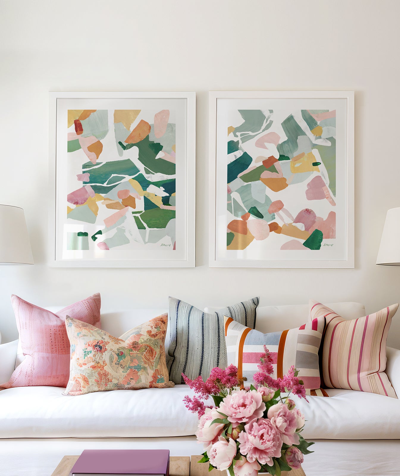 A bright, white living room with a white sofa and colorful pillows featuring two, framed, colorful, abstract, artworks above the sofa.