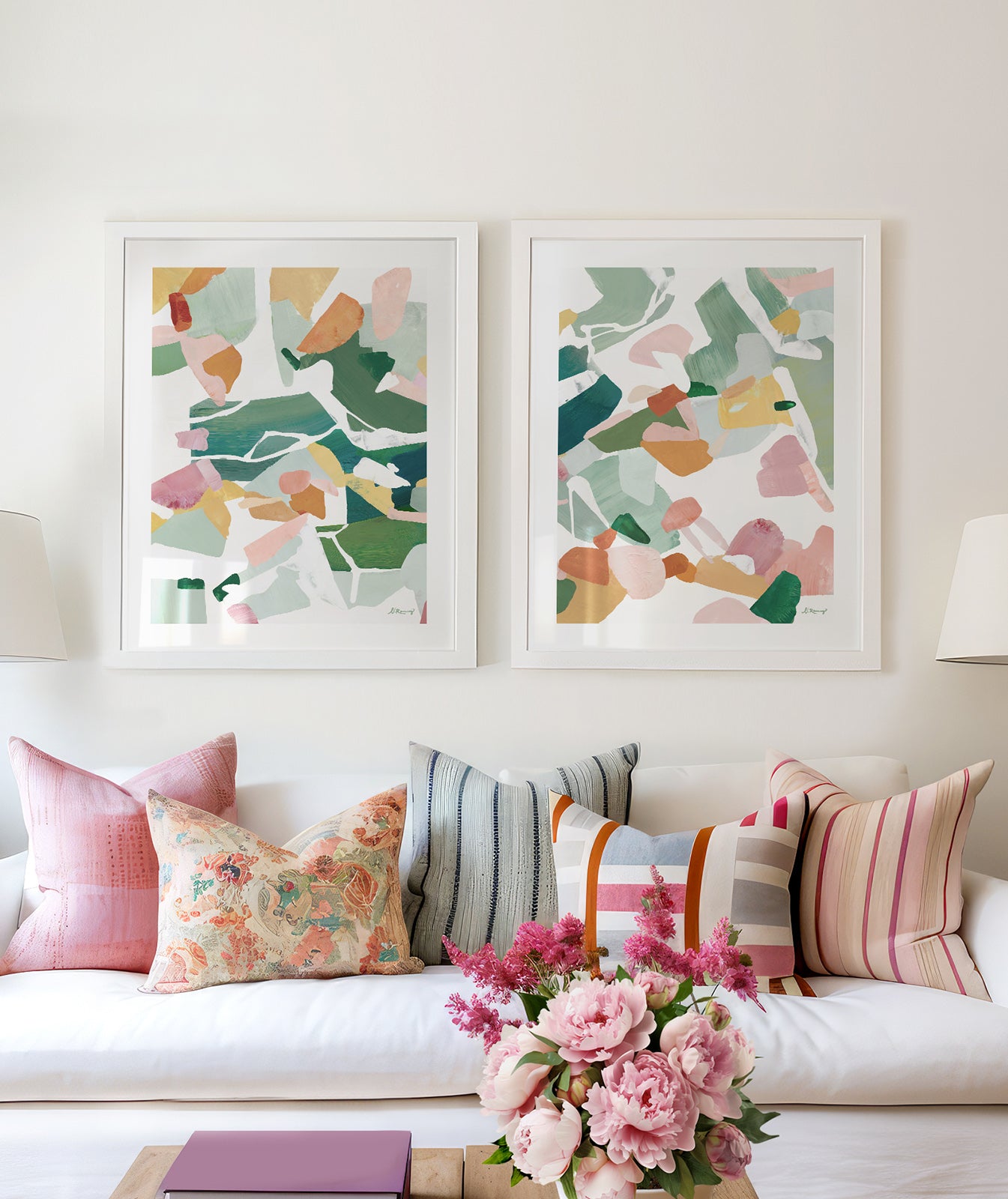 Living room with a white sofa, colorful pillows, and two framed abstract art prints in green, orange, pinks and yellow tones on the wall.