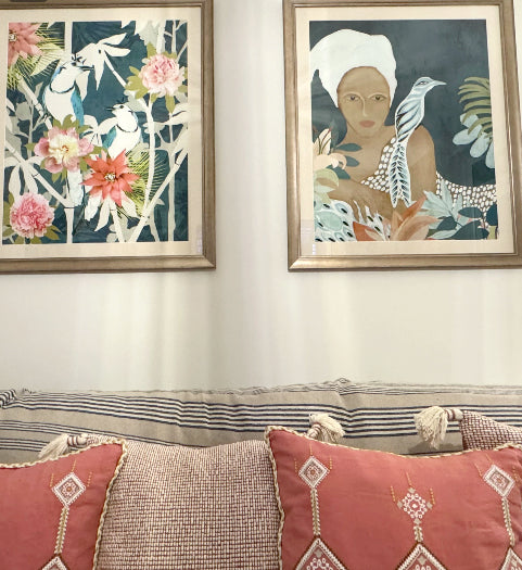 Two framed art prints titled "Lounging" and "Sweet Chinoiserie" featuring birds in a garden scene along with a woman displayed in gold frames above a sofa.