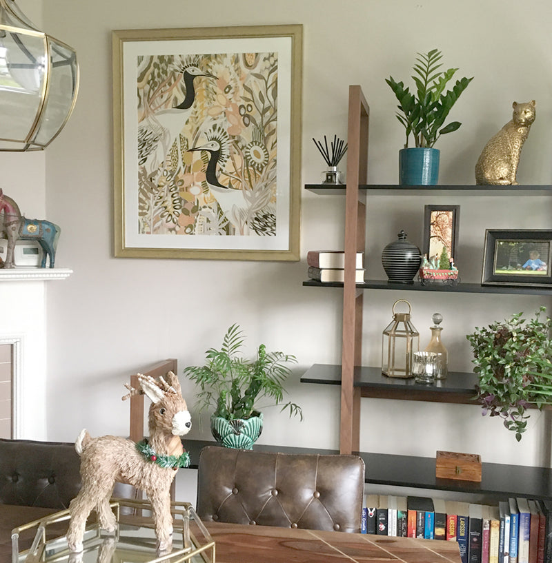 Customer photo of artwork titled Garden Stroll featuring two black and white crane birds in a colorful abstract garden featuring shades of yellow, pink and muted green. The artwork is framed in gold and displayed in a dining room.