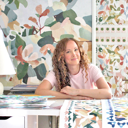 The artist Nancy Ramirez sitting in her studio with her colorful floral artwork in the background.