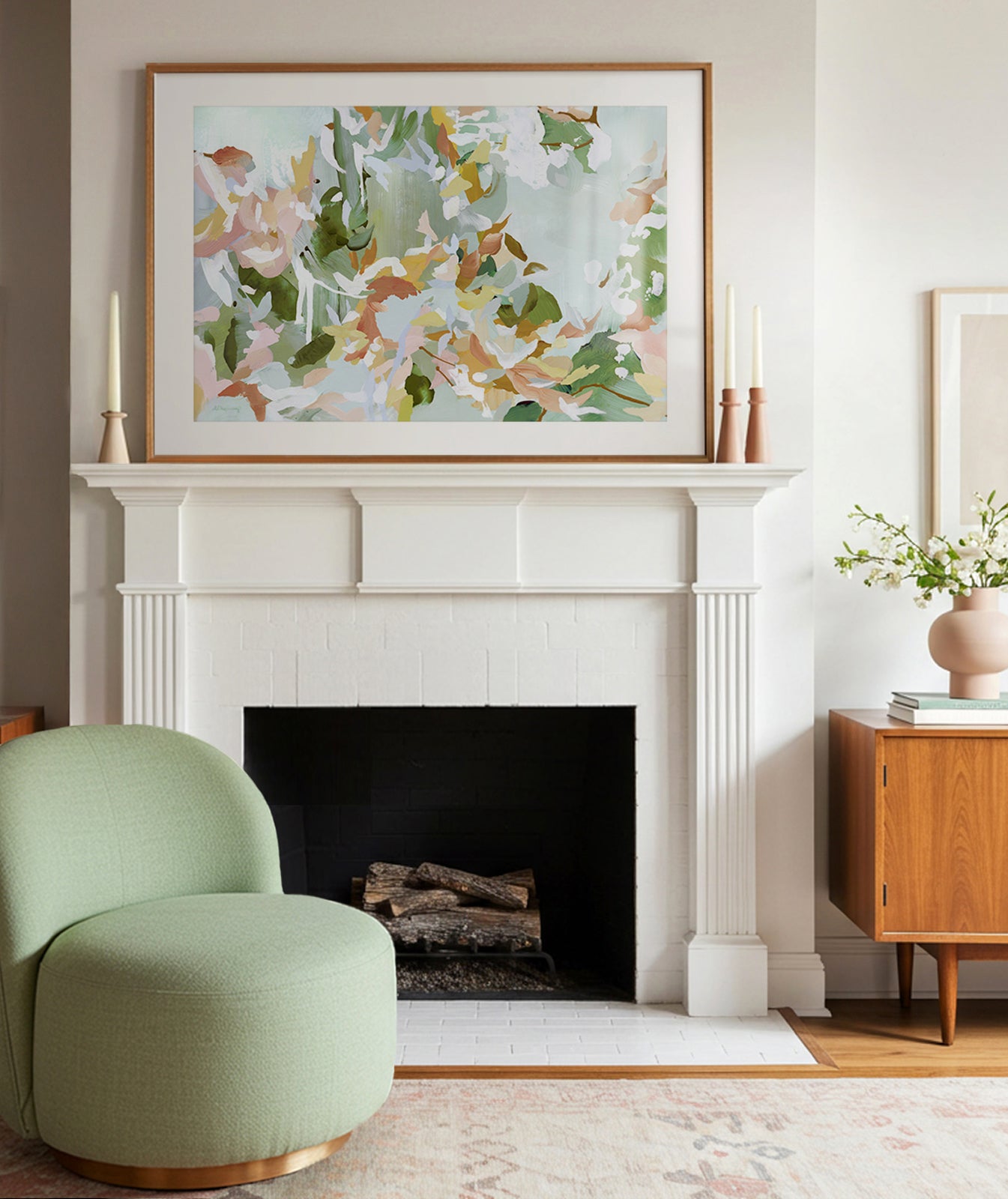 A framed abstract artwork above a fireplace, with layered brushstrokes in greens, burnt umber, and pinks, representing plant life.