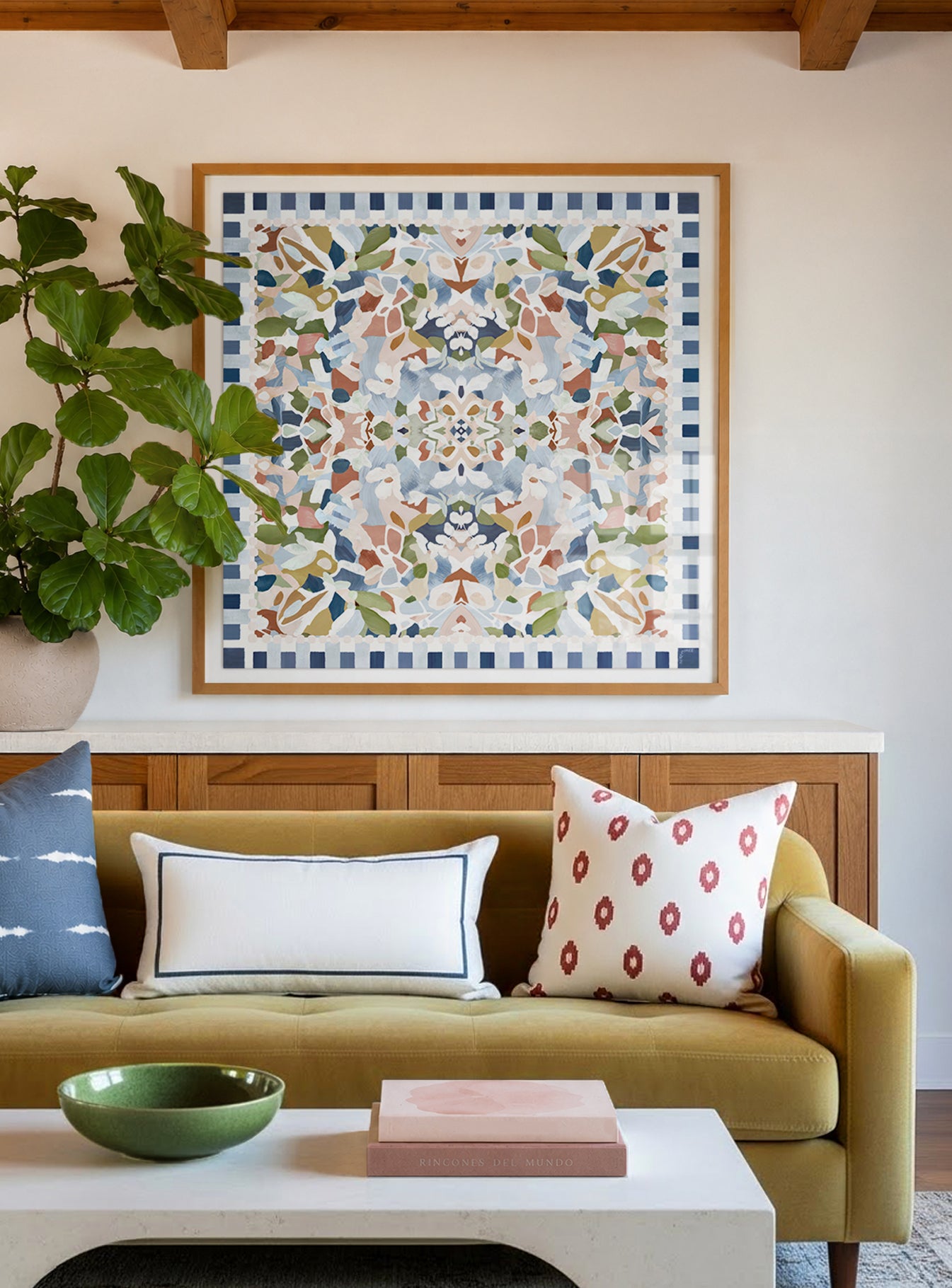 A large-scale square artwork featuring an abstract and floral pattern in muted blues, pinks, yellow and green featured framed above a muted yellow sofa.