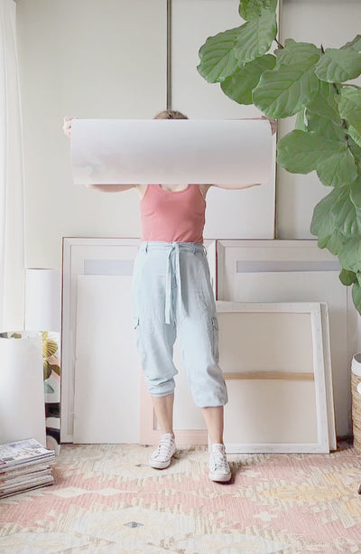 A woman standing in a room holding a colorful, abstract poster print in various colors.