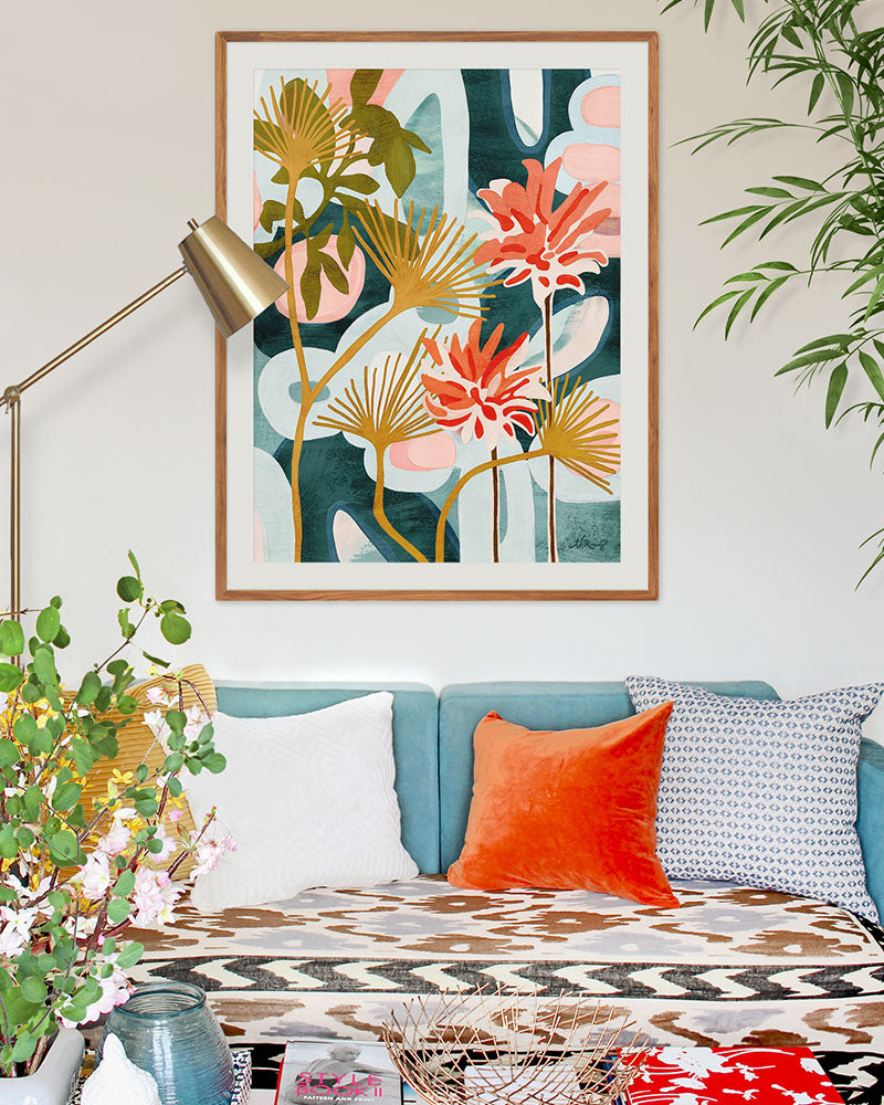A framed, abstract floral art print displayed on a wall above sofa. The artwork features red, green, yellow, light blue and dark blue.